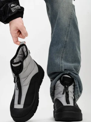 Black and grey mid-calf zip-up snow boots worn with blue jeans, showing quilted padding, chunky platform sole, and urban streetwear styling