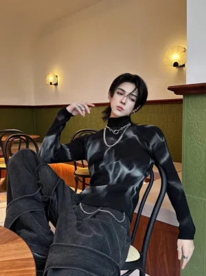 Male model wearing a black and grey tie-dye ribbed turtleneck sweater with wide-leg denim pants in a retro cafe streetwear setting