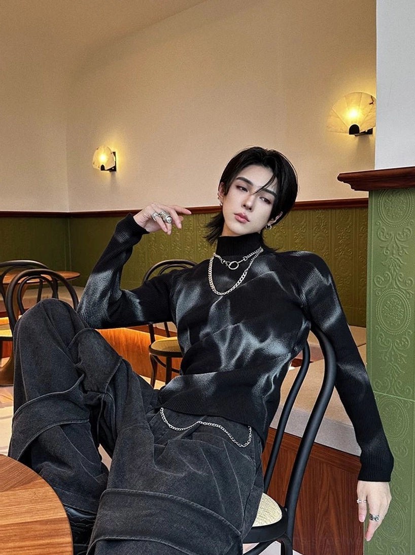 Male model wearing a black and grey tie-dye ribbed turtleneck sweater with wide-leg denim pants in a retro cafe streetwear setting