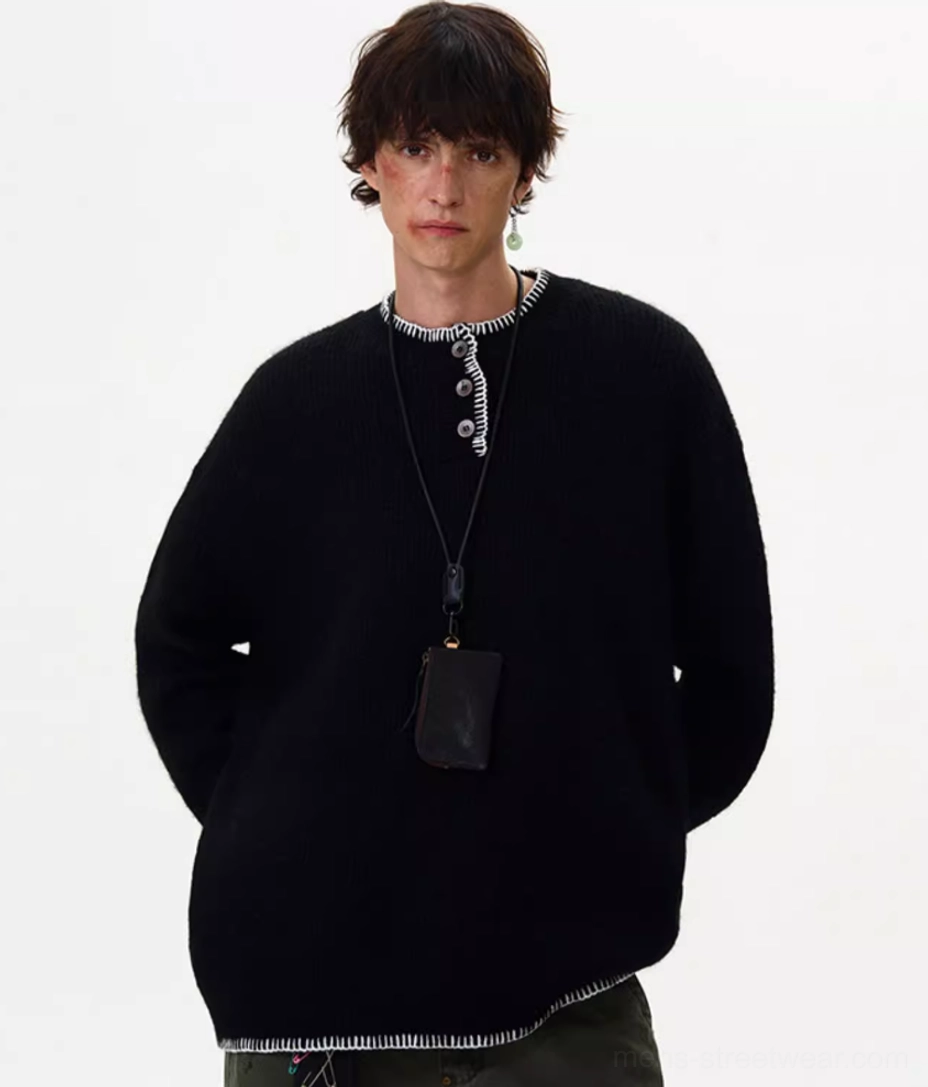 Upper-body view of black oversized knit sweater with white contrast stitching, buttoned Henley neckline, and streetwear accessories