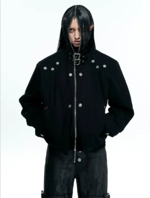Black high neck hardware canvas jacket worn by male model in a minimalist studio, featuring silver rivet details and buckle collar