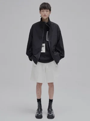 Black high-neck structural windbreaker jacket styled with a dark top, white shorts, and black boots
