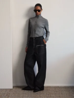 High rise black baggy utility jeans with white contrast topstitching shown in a front full-body minimalist studio look