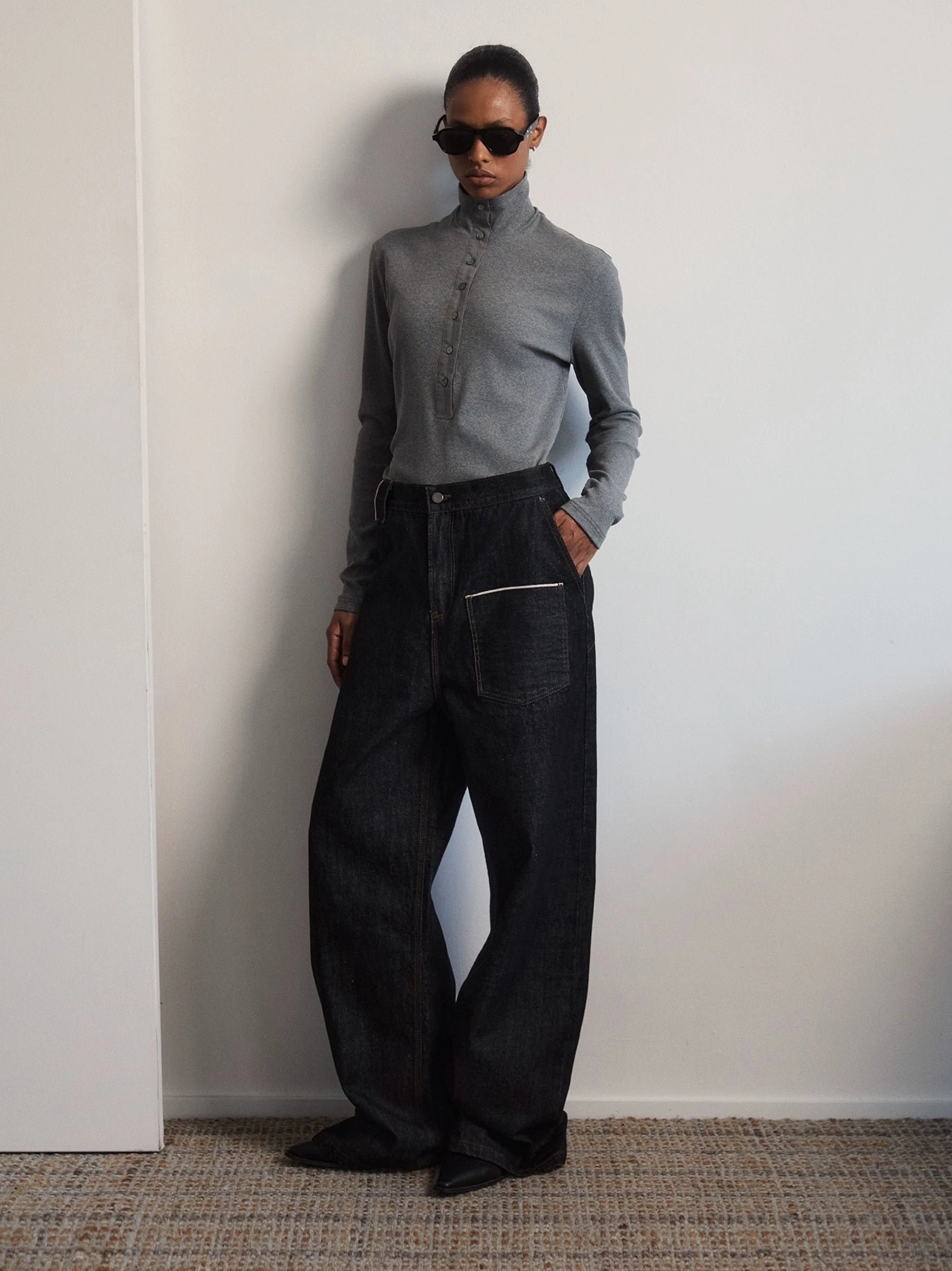 High rise black baggy utility jeans with white contrast topstitching shown in a front full-body minimalist studio look