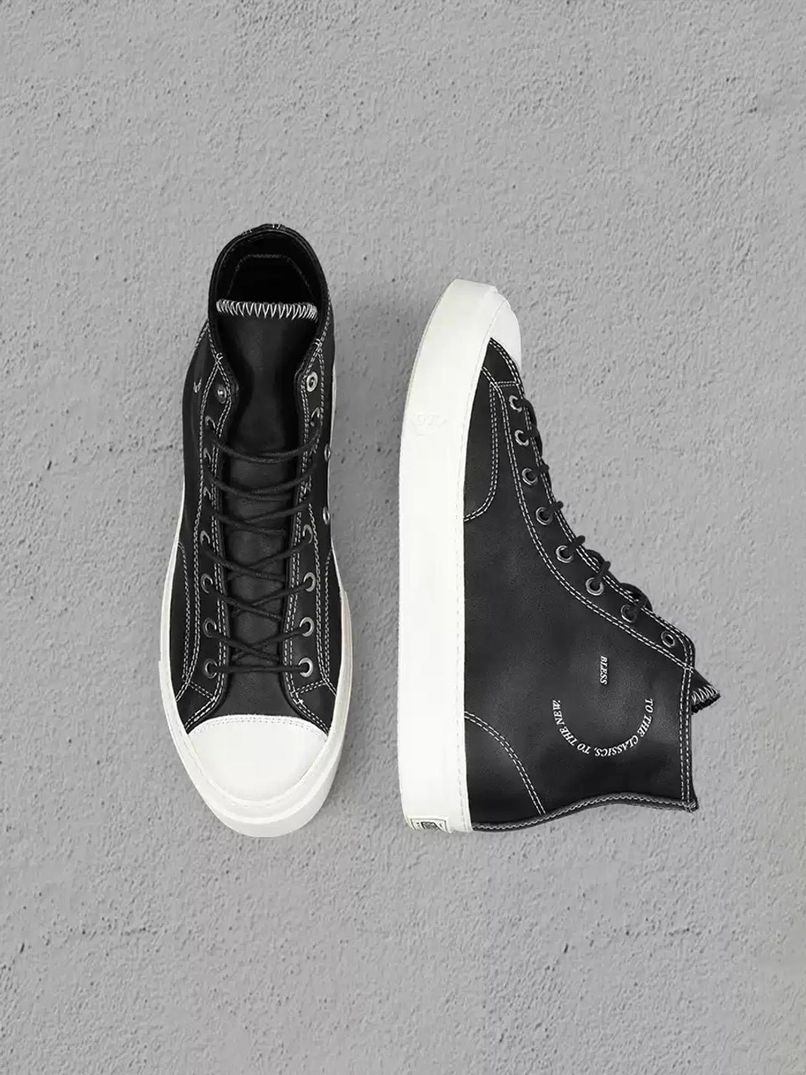 Top-down view of matching black high-top streetwear sneakers with white toe caps, contrast collar stitching, printed side details, and platform soles