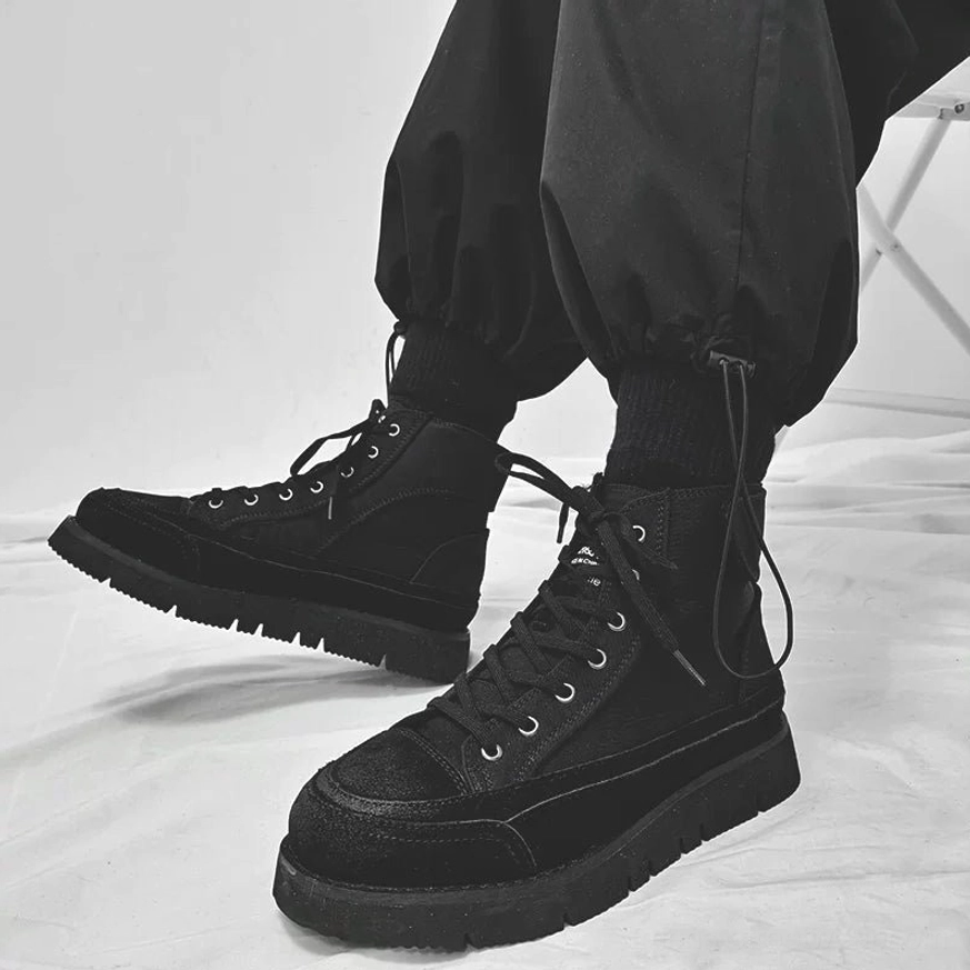 Black high-top work boots with suede toe cap, rear heel strap, textured lugged outsole, and cargo pants styling