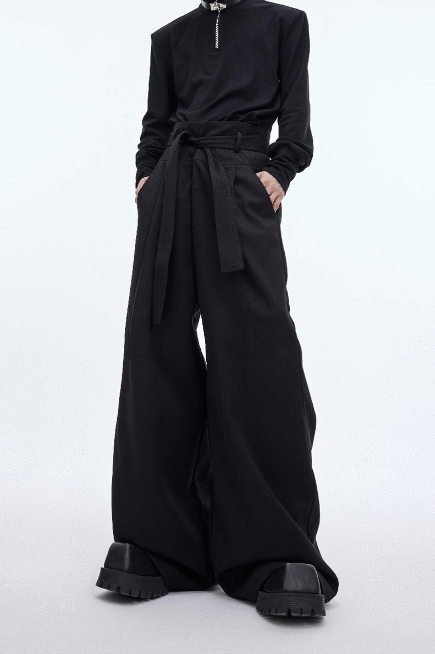 Black high-waist draped wide-leg streetwear trousers with attached waist sash styled with black half-zip top and platform boots