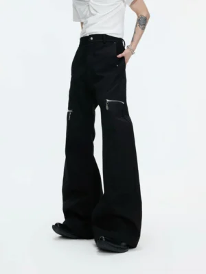 Male model wearing black high waist wide leg pants with silver metal zip thigh pockets in a white studio front full body view