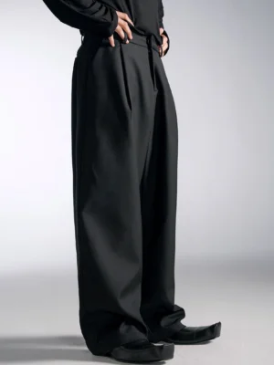 Black high-waist wide-leg pleated trousers with oversized tailored streetwear silhouette shown in a low front close-up