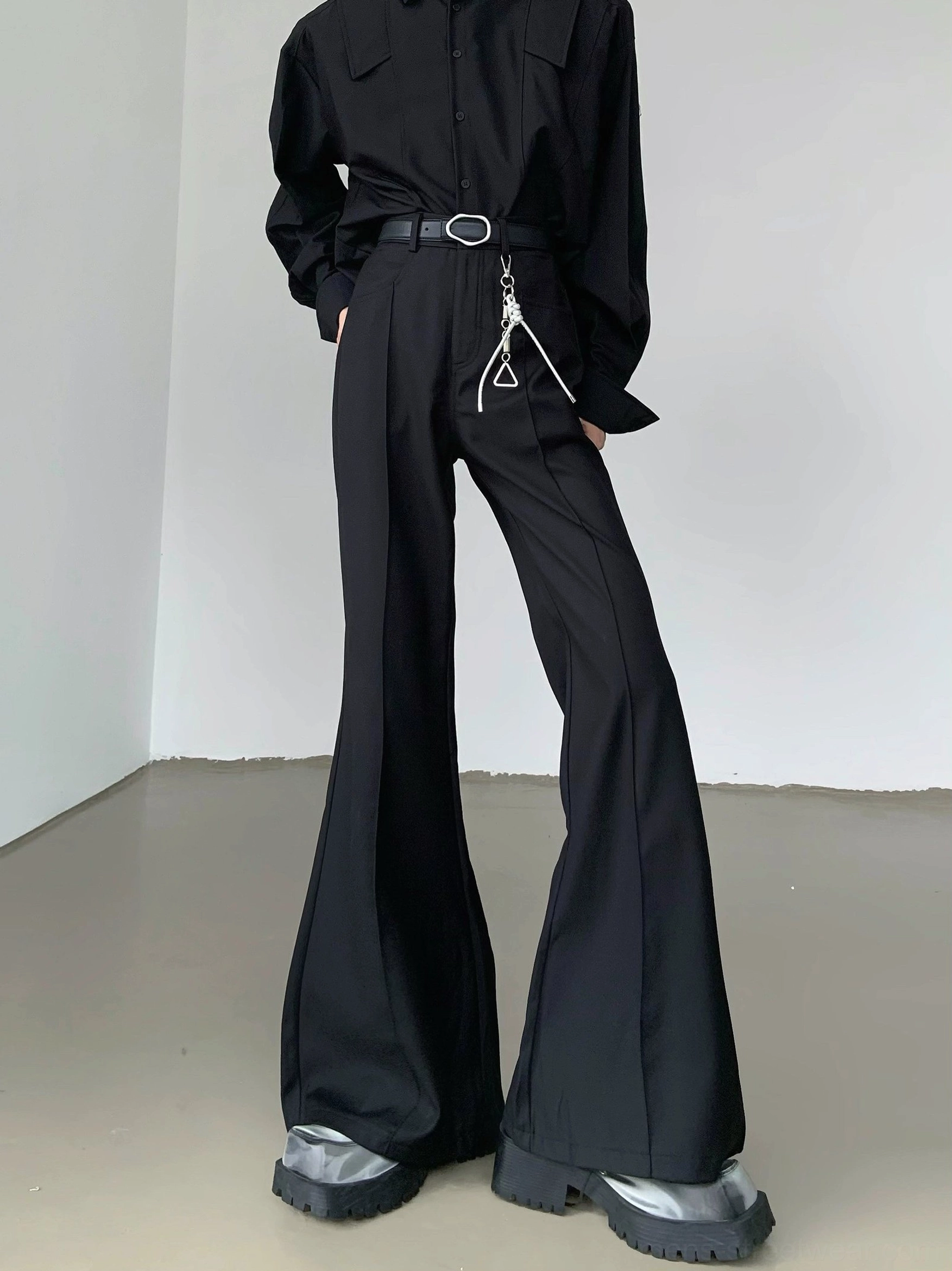 Black high-waisted flare trousers with sharp front crease, wide bell-bottom legs, oval buckle styling, and avant-garde Seoul fashion silhouette