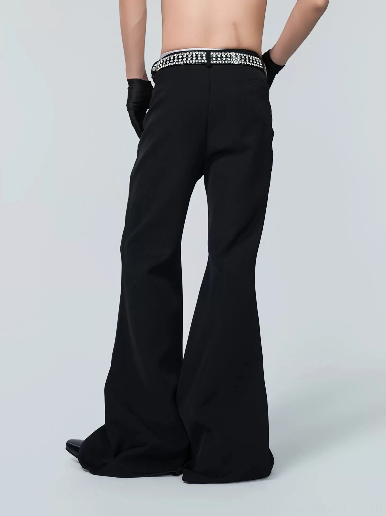 Rear full-body view of black high-waisted flared trousers with a clean back, wide floor-length legs, tailored shape, and studded belt