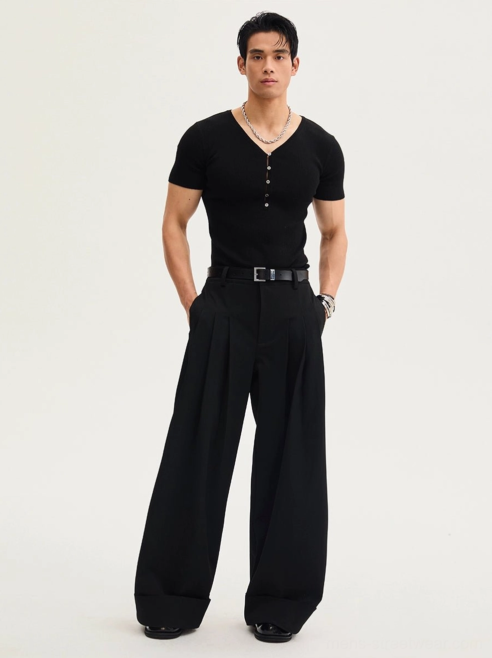 Full-body male model wearing black high-waisted oversized pleated trousers with wide legs, rolled cuffs, leather belt styling, and contemporary Korean fashion look