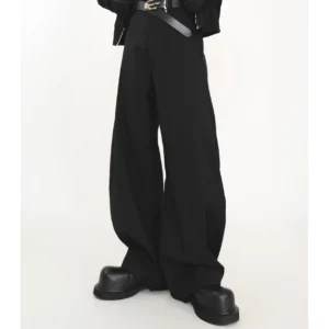 Close-up low-angle view of oversized black high-waisted wide-leg streetwear trousers with flowing fabric, wide belt, and chunky black leather shoes