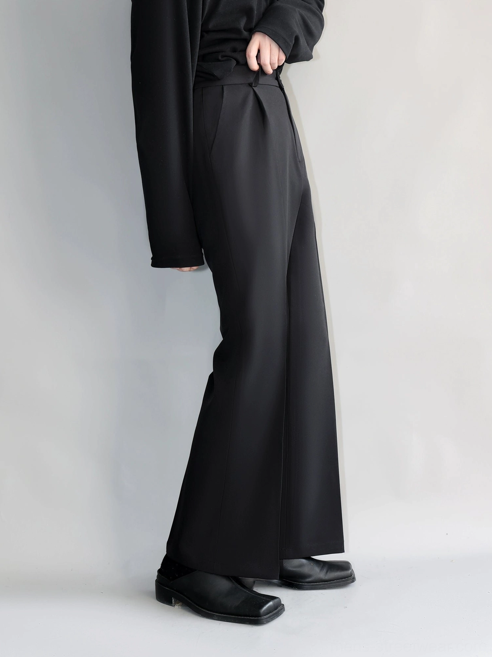 Black high-waisted relaxed straight-leg trousers with subtly flared hem shown from the side in minimalist studio styling