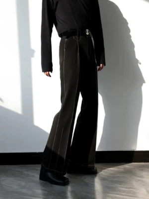 Rear side view of black high-waisted tailored flared trousers with white contrast topstitching styled with a black streetwear outfit and leather shoes