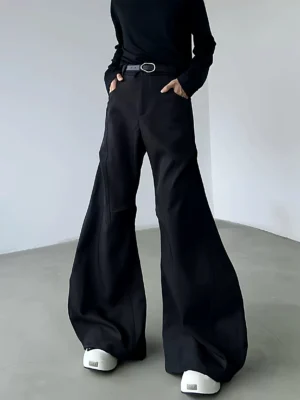 Black high-waisted ultra-flare streetwear trousers with sculpted curved legs, oval buckle belt, matte fabric, and floor-length silhouette styled with chunky shoes