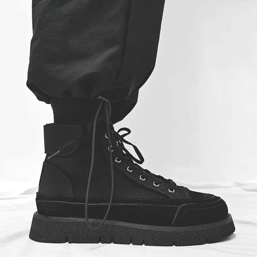 Black high-top Japanese streetwear work boots with mixed suede and canvas upper, chunky anti-slip rubber sole, and black tapered cargo pants