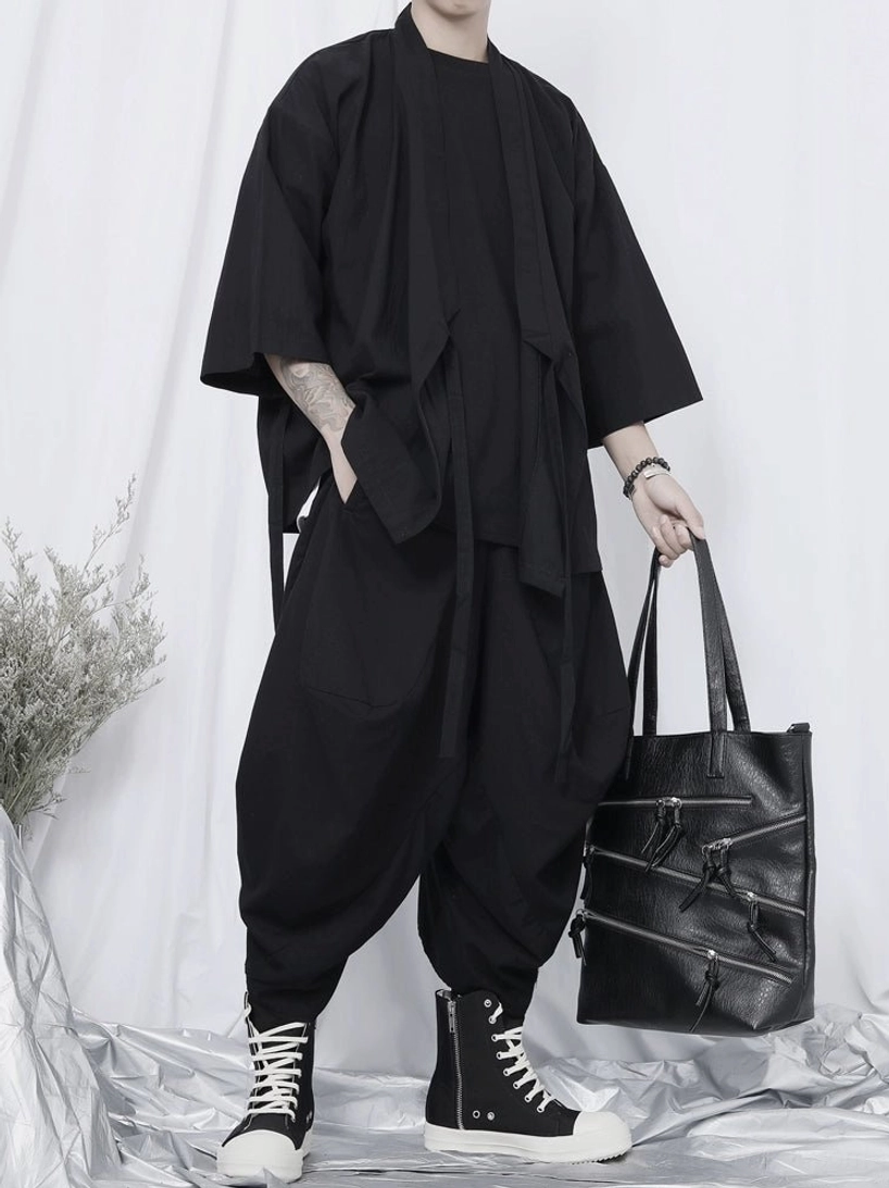 Side view of oversized black kimono shirt styled with cropped harem pants, high-top sneakers, wrist accessories, and a leather tote bag