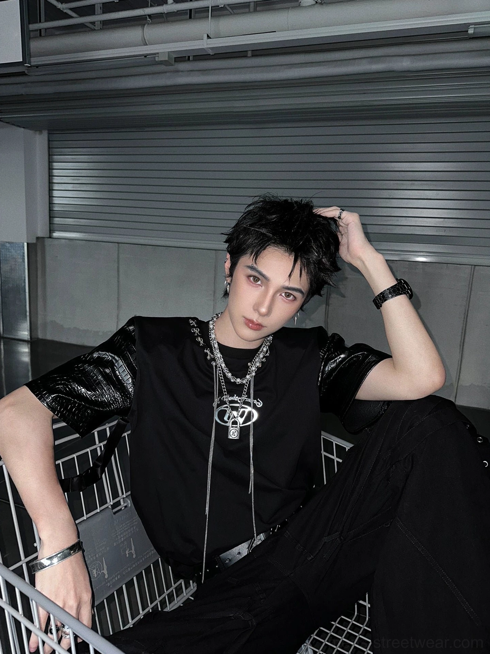 Black Korean streetwear panel T-shirt with crocodile-textured faux-leather sleeves and layered silver necklaces in an industrial interior