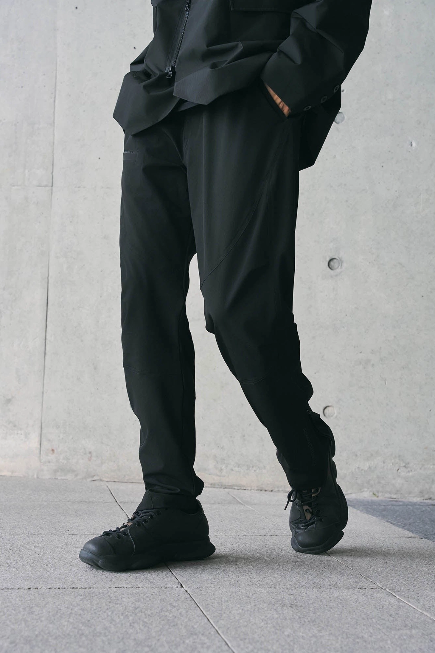 Three-quarter front view of black Korean techwear track pants with relaxed straight leg fit and ankle zipper details