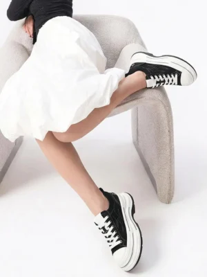Model wearing black layered platform canvas sneakers with a white ruffled skirt, showing the chunky low-top streetwear silhouette