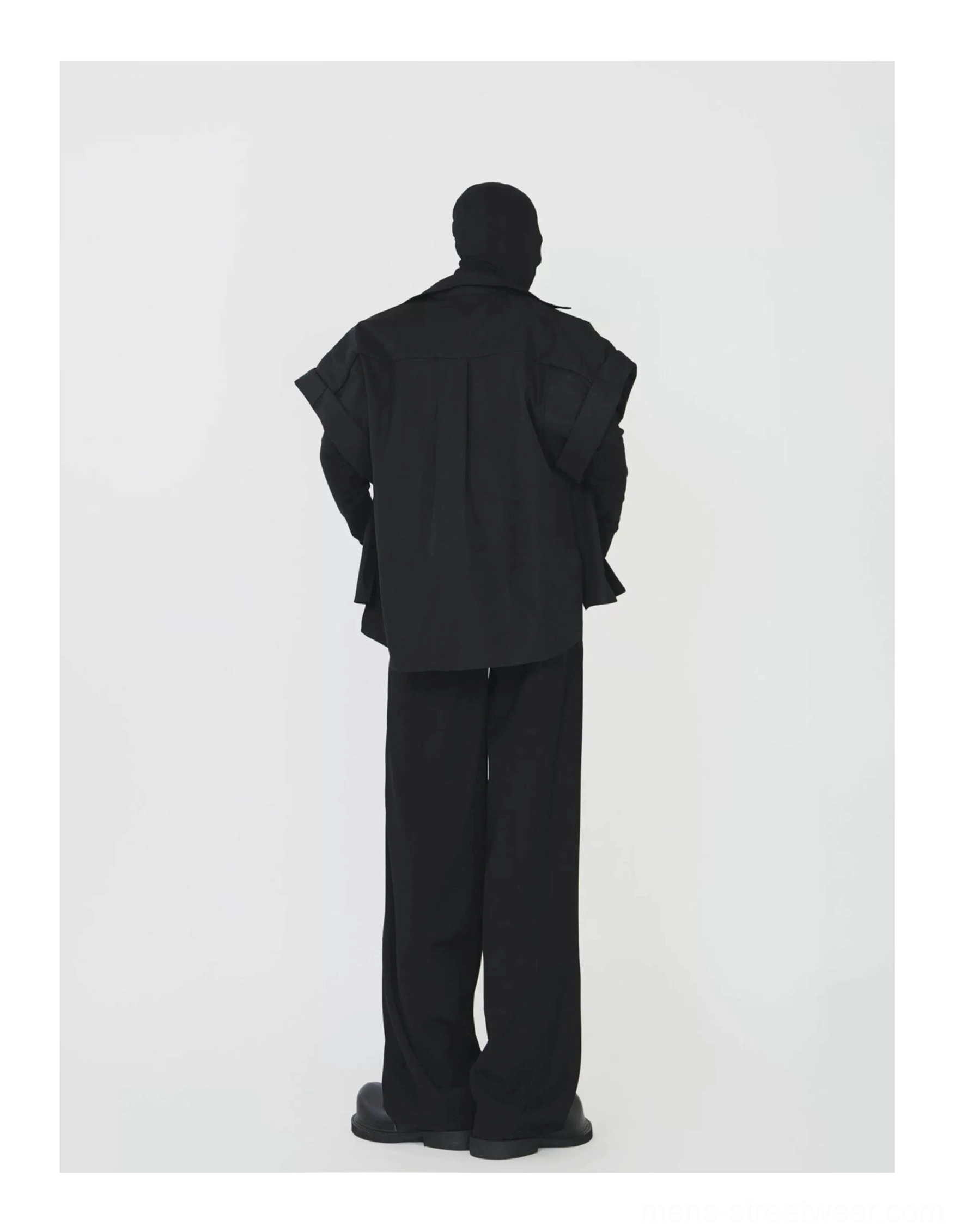 Rear side view of a model wearing a black layered streetwear shirt jacket with a flowing oversized back silhouette