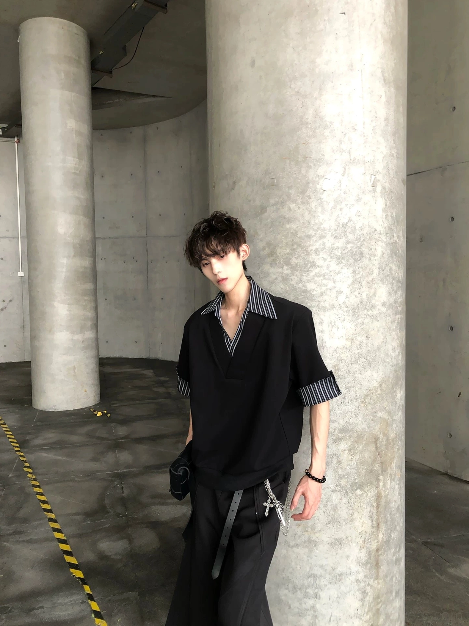 Side view of black oversized V neck shirt with contrast striped cuffs styled with chain detail streetwear trousers