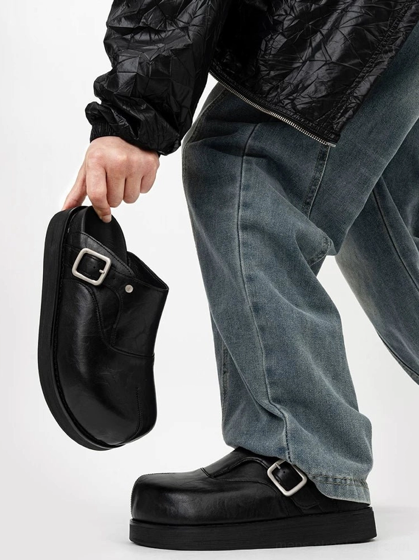 Black leather buckle mule worn with baggy jeans and a black jacket showing the adjustable outer instep strap and thick platform sole