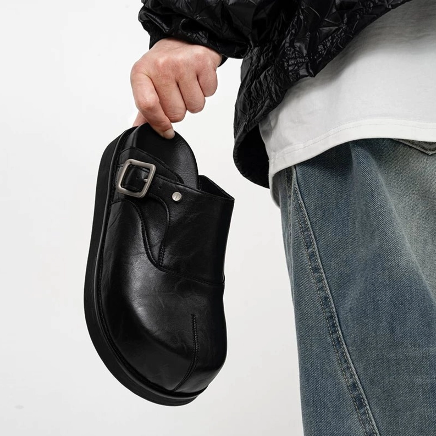 Front three-quarter view of polished black leather buckle mules styled with a cropped white top black jacket and baggy jeans