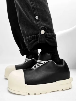 Black leather chunky platform sneakers with cream sole and white laces shown in side profile with rolled black denim