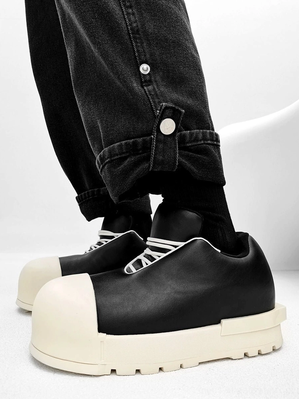 Black leather chunky platform sneakers with cream sole and white laces shown in side profile with rolled black denim