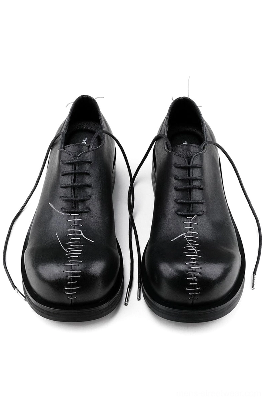 Pair of black leather Oxford shoes viewed from above showing black laces, polished cowhide uppers, and bold white center toe stitching