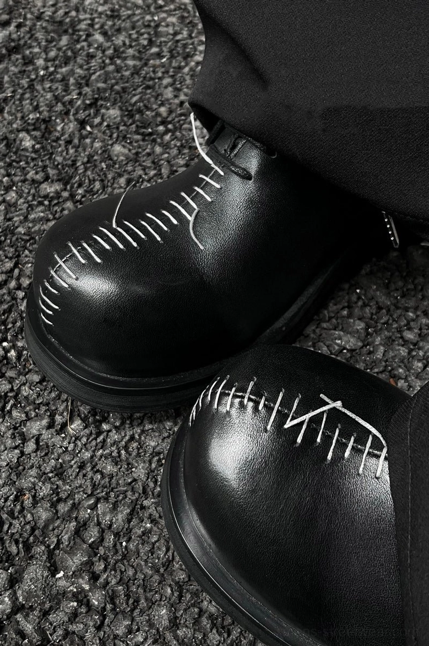 Close-up of handcrafted white contrast stitching on the rounded toe of polished black leather Oxford shoes