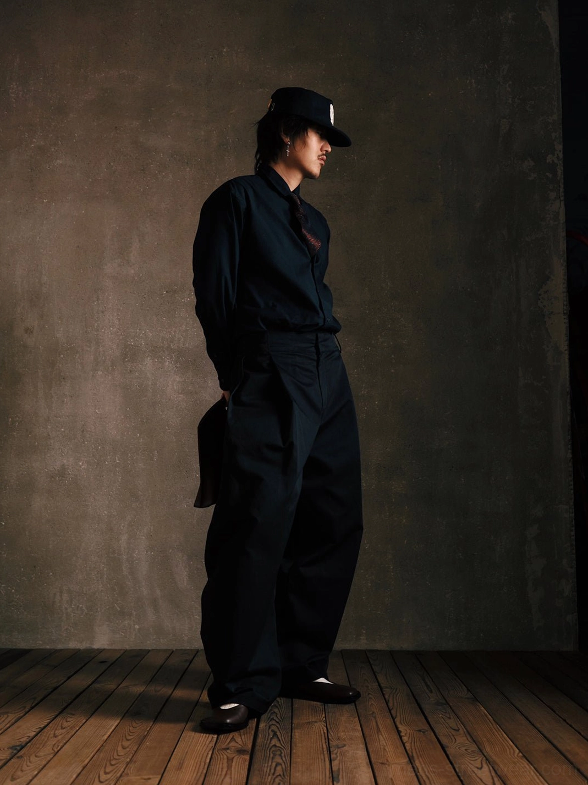 Full-length view of black leather Mary Jane shoes paired with a tailored black outfit and baseball cap in a minimalist fashion studio