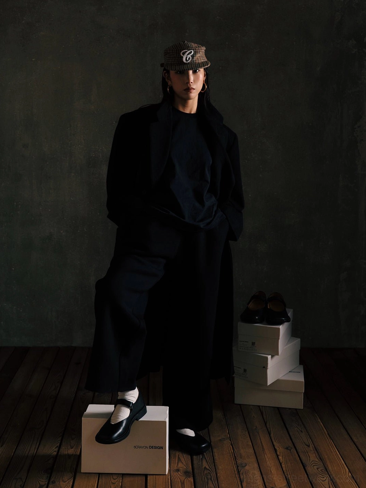 Male model wearing black leather Mary Jane shoes with an all-black tailored outfit and plaid baseball cap in a contemporary streetwear studio