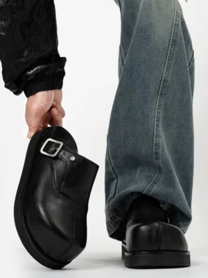 Rear view of black leather platform buckle mules with chunky rubber sole styled with loose blue jeans and a quilted jacket for Korean streetwear