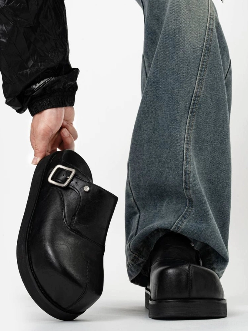 Rear view of black leather platform buckle mules with chunky rubber sole styled with loose blue jeans and a quilted jacket for Korean streetwear