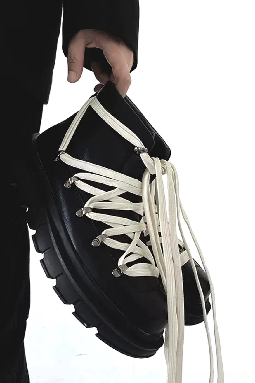 Front view of paired black leather platform combat boots with contrast laces styled in all-black streetwear outfit