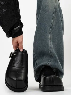 Front side view of black leather platform mules showing stitched upper panels silver buckle hardware and chunky flat sole