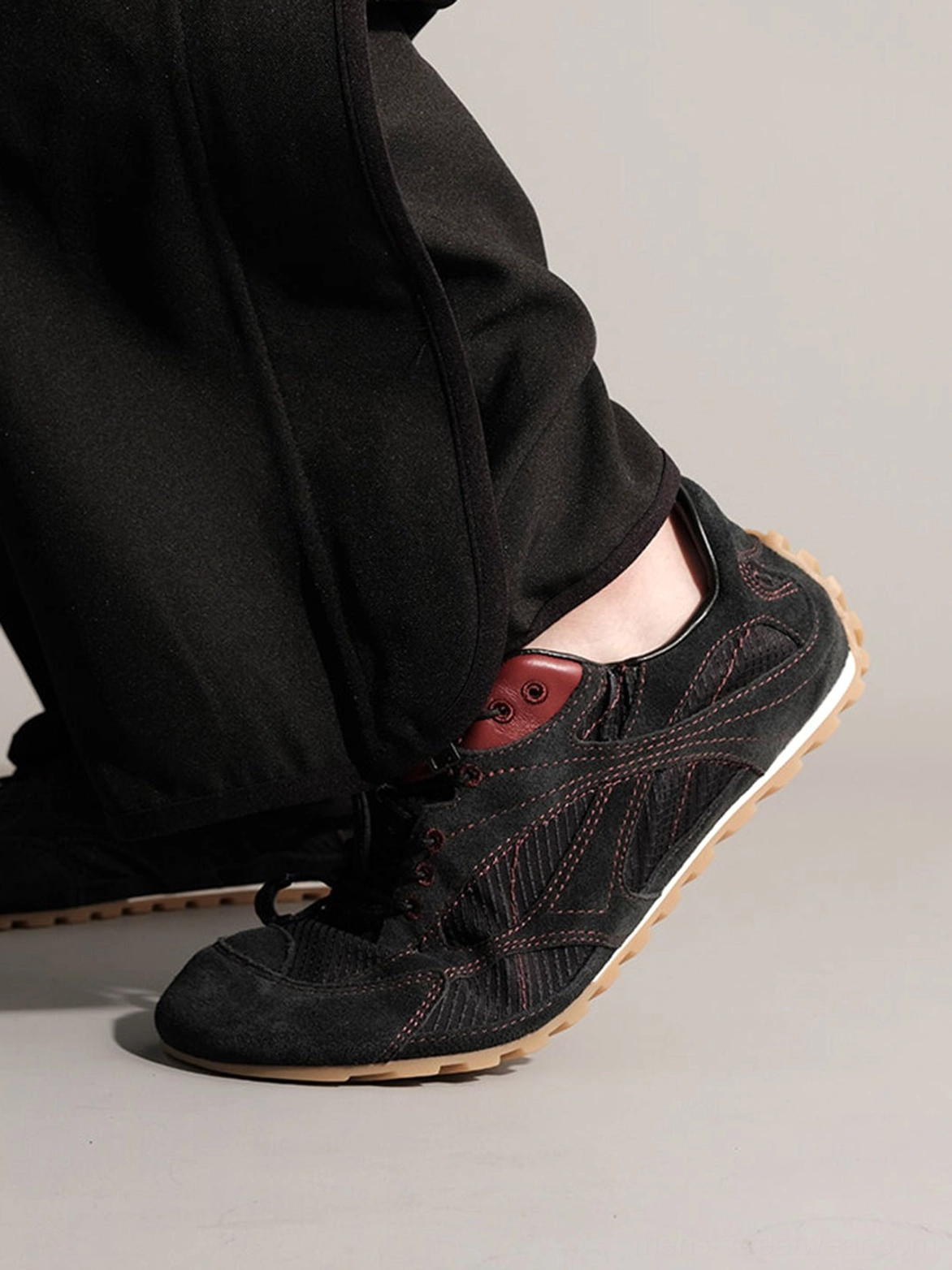 Black low-profile nubuck sneakers with red contrast stitching and exposed maroon insole shown from a low side angle