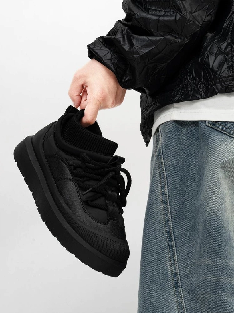 Side profile of black low-top knit collar platform sneakers with smooth paneled upper, rear pull tab, flat laces, and chunky rubber sole