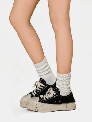 Back view of black low-top platform canvas sneakers styled with white crew socks and a cracked distressed rubber sole