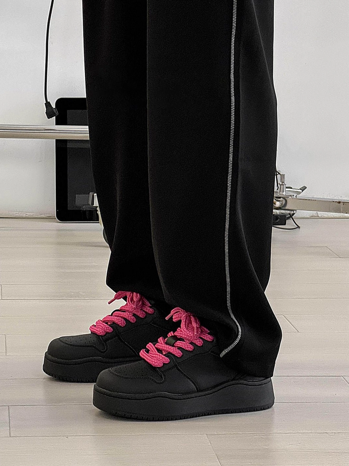 Low angle front view of black low top platform sneakers with hot pink laces and wide leg pants