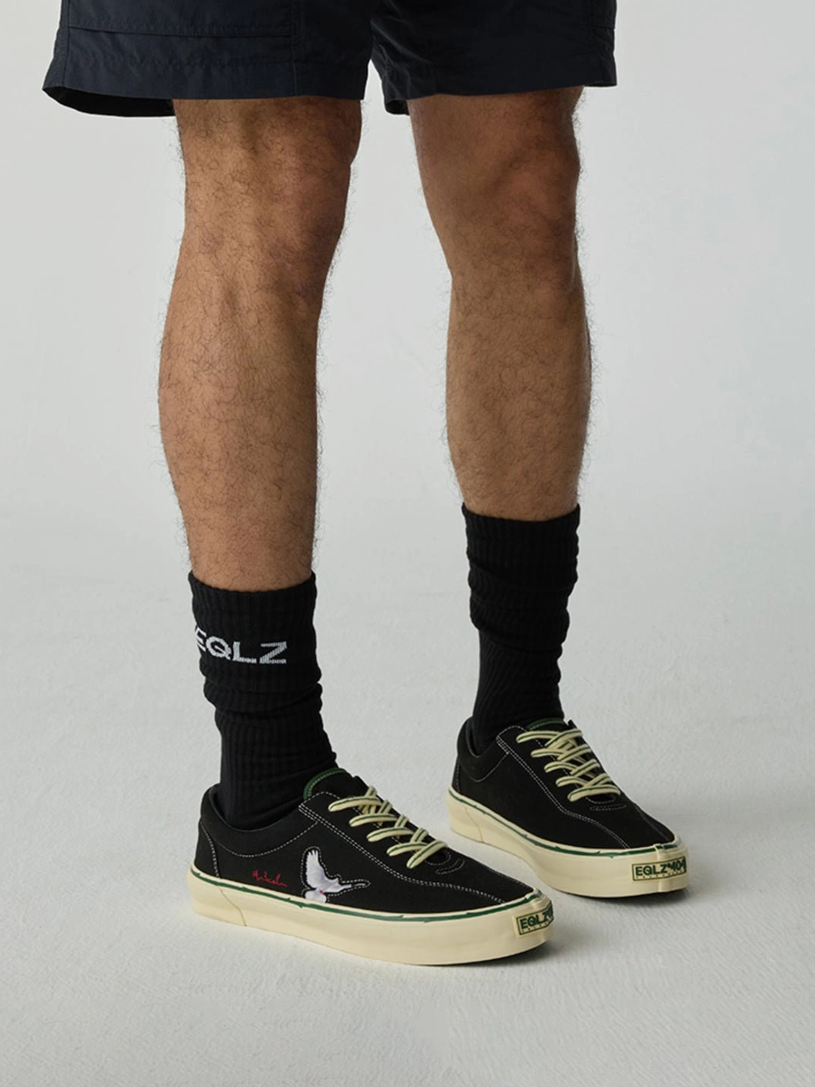 Male model wearing black low-top skate shoes with a contrasting embroidered dove motif and off-white midsoles