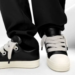 Front and rear view of black low-top thick sole sneakers with polished leather finish, off-white color-blocked toe cap, and modern streetwear styling