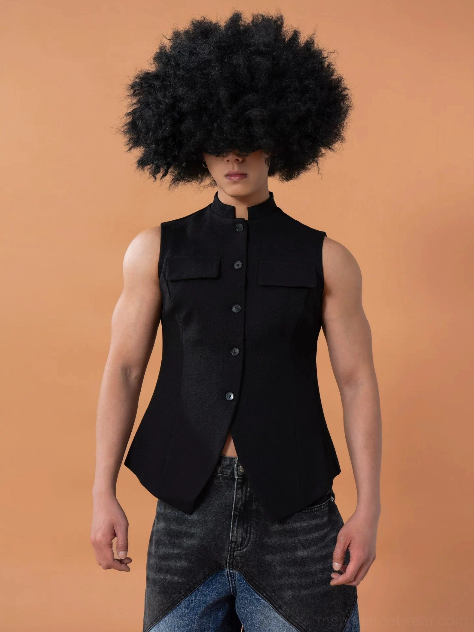 Front full view of a black mandarin collar tailored vest with sculpted shoulders, fitted waist, button closure, chest flap pockets, and pointed split hem styled with wide-leg denim