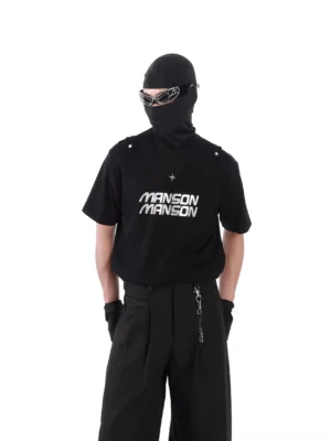 Black MANSON graphic utility T-shirt styled with tactical techwear outfit, shoulder tab details, silver cross pendant, gloves, sunglasses, and wide-leg trousers
