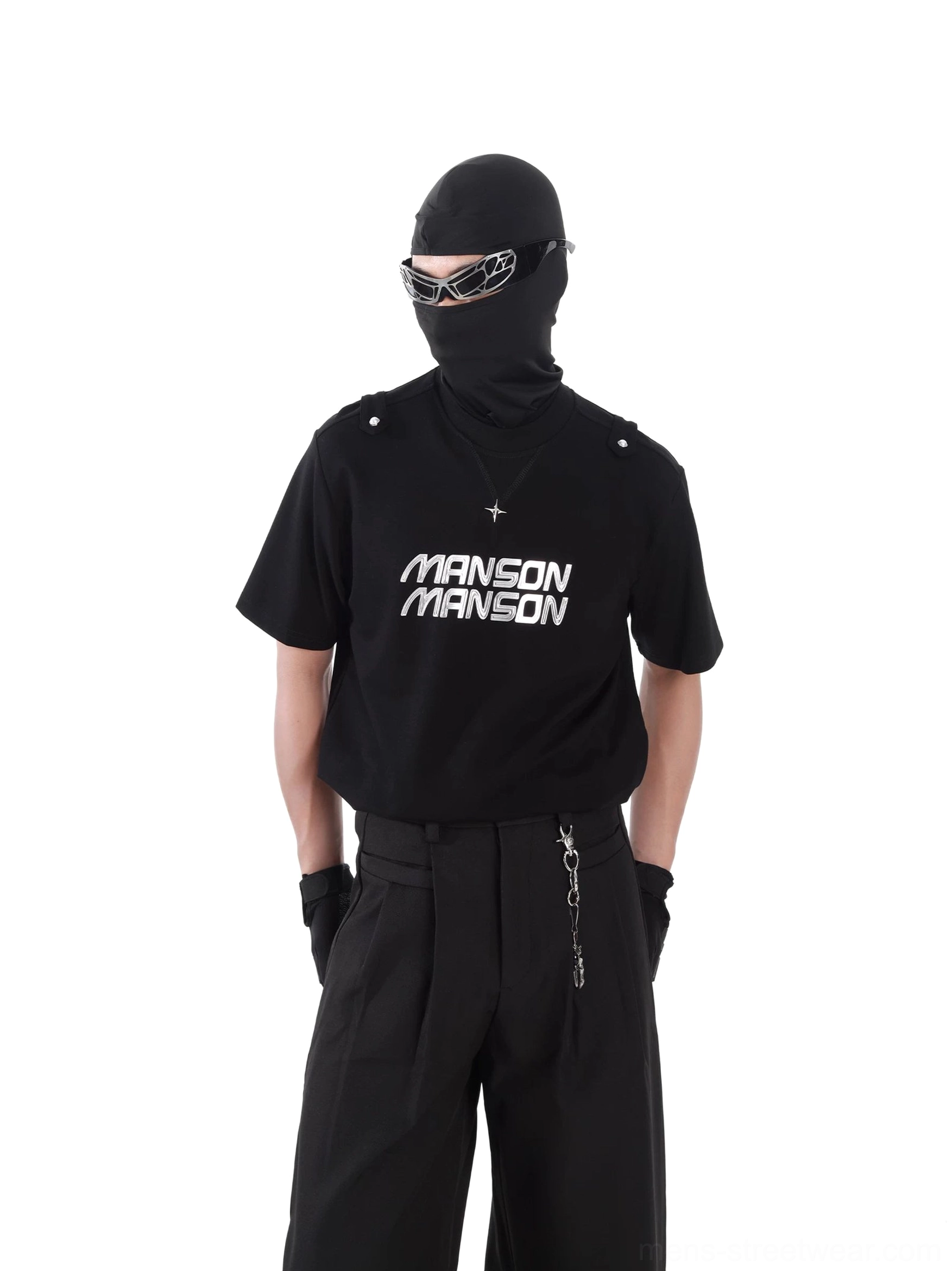 Black MANSON graphic utility T-shirt styled with tactical techwear outfit, shoulder tab details, silver cross pendant, gloves, sunglasses, and wide-leg trousers
