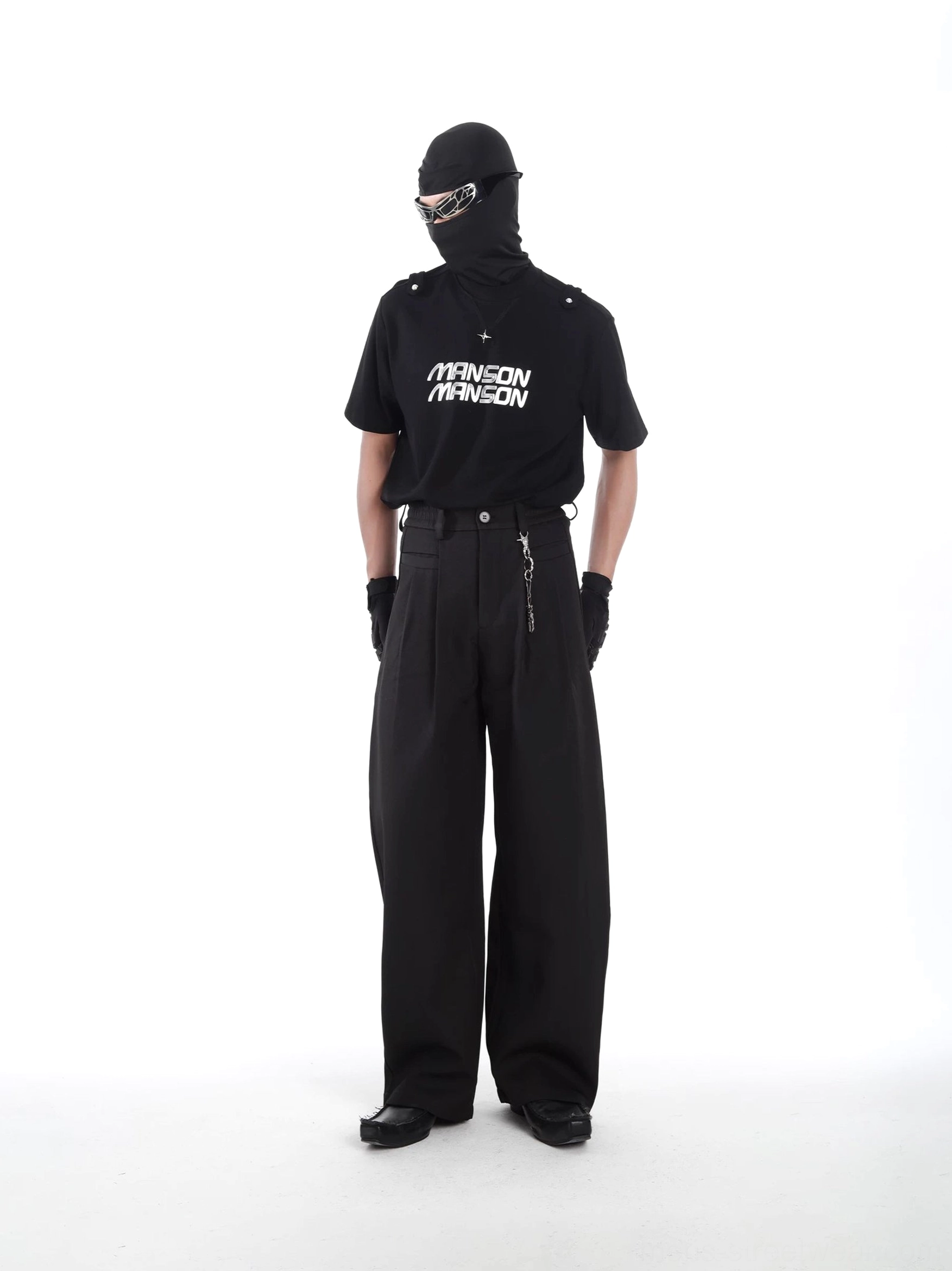 Side three-quarter view of black MANSON utility tee paired with wide-leg tailored trousers, shoulder epaulets, waist chain, and techwear accessories