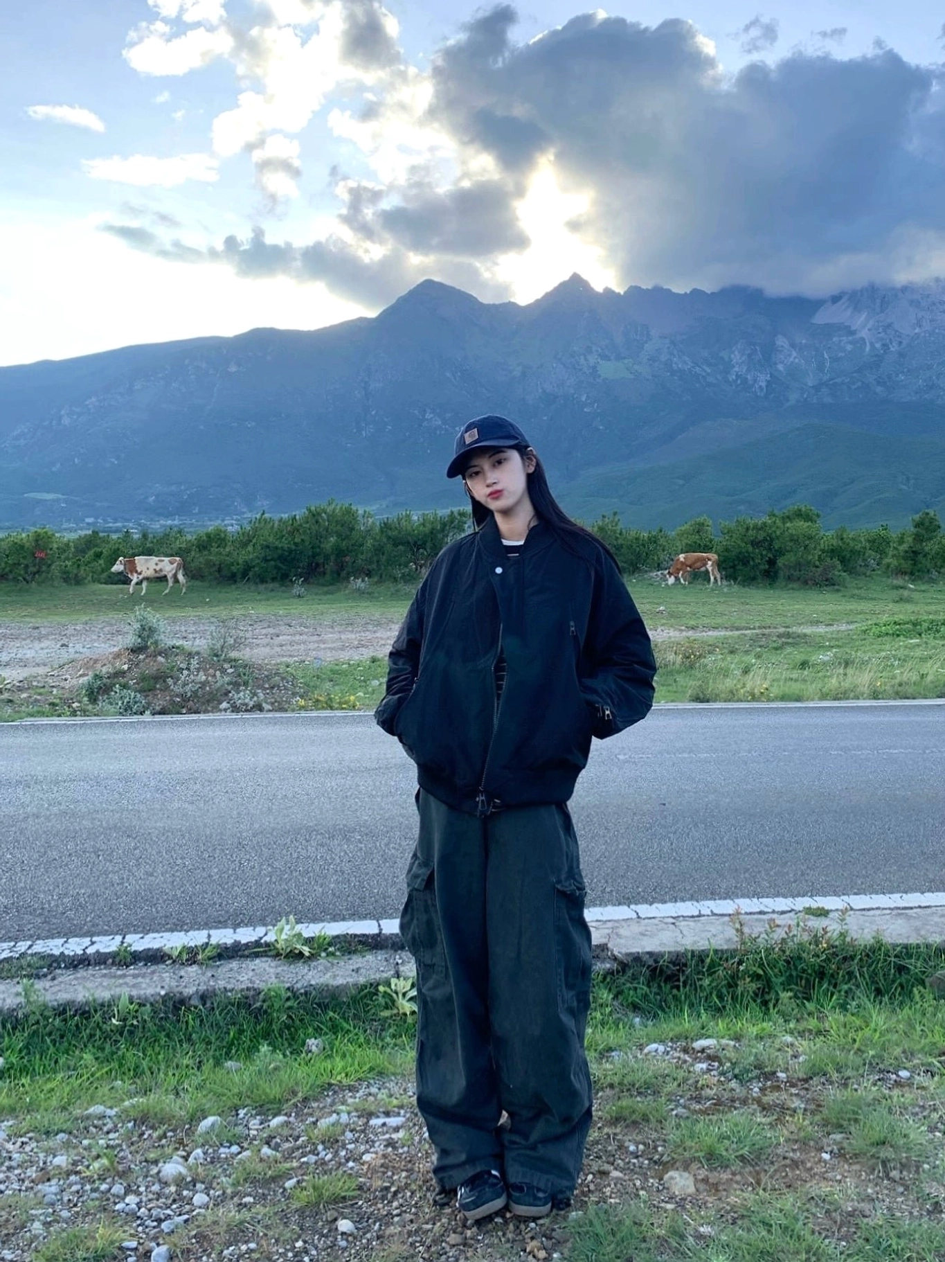 Black matte oversized bomber jacket three-quarter view styled with cap and wide-leg cargo pants